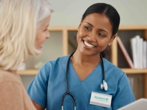 A picture of a female healthcare worker talking to a female patient, whilst using an electronic device.
