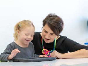 A picture of a child with a female education worker on an electronic device.