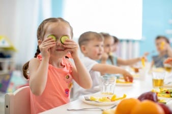 An image of a young girl holding slices of cucumbers to her eyes whilst eating a school meal.